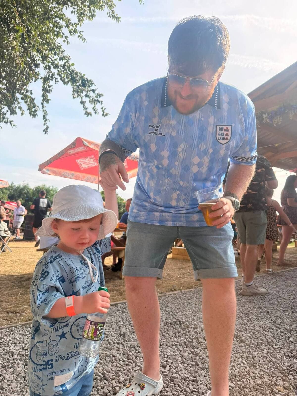 A dad and his toddler in a sun hat sharing a drink at The Comfortable Gill Garden Party