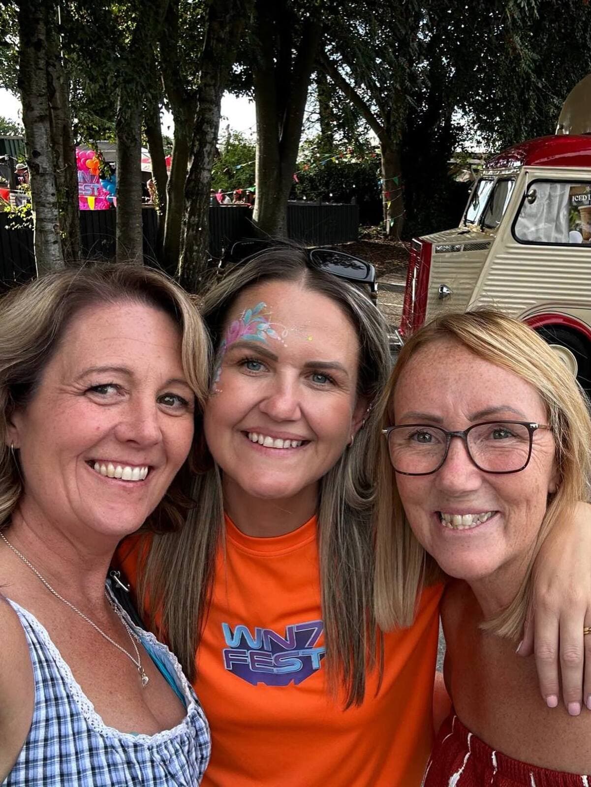 Three friends with glitter face paint in WN7 FEST shirts at the Garden Party