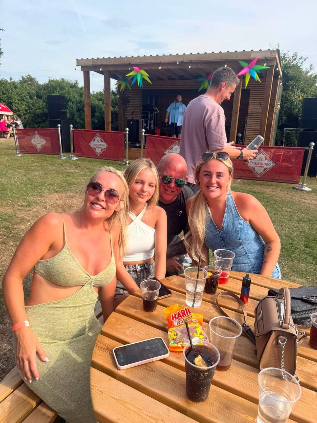 A family at a picnic table with the stage behind them at the Garden Party