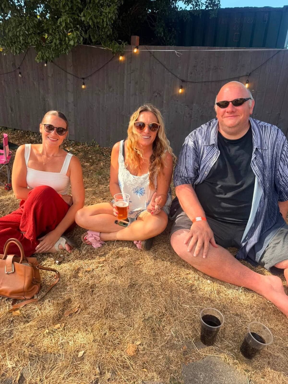 Friends sitting on the grass under festoon lights at golden hour, WN7 FEST Garden Party